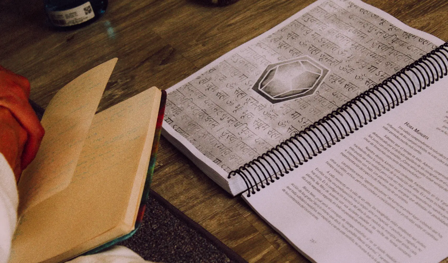 Manual de enseñanza abierto en una página con mantras en sánscrito, junto a un cuaderno de apuntes
