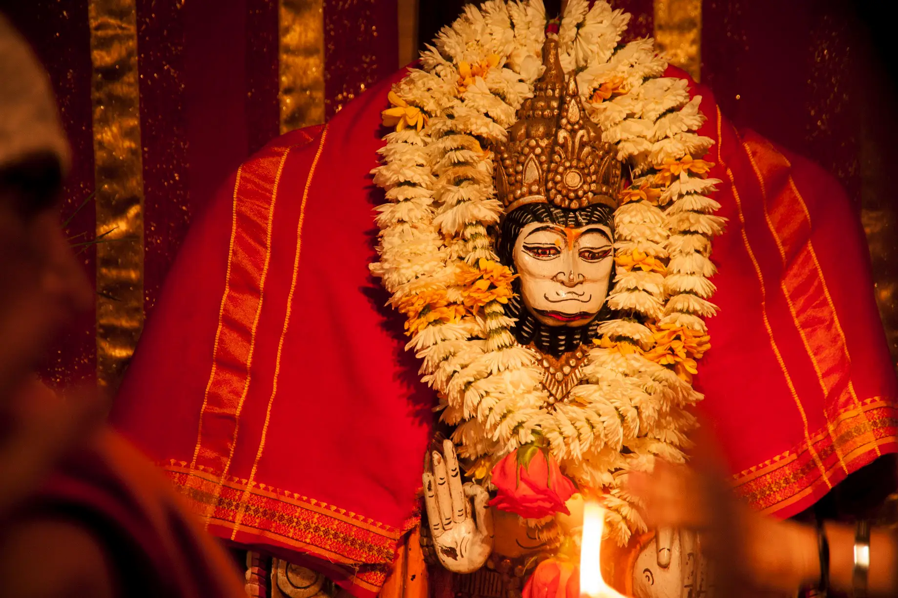 Murti de Hanuman con guirnaldas de flores y vela encendida